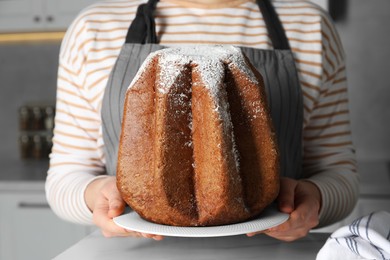 Photo of Woman holding delicious Pandoro cake decorated with powdered sugar in kitchen, closeup. Traditional Italian pastry