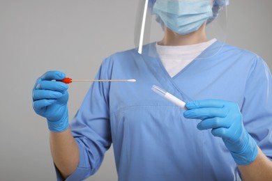 Photo of Laboratory testing. Doctor with cotton swab and tube on light grey background, closeup