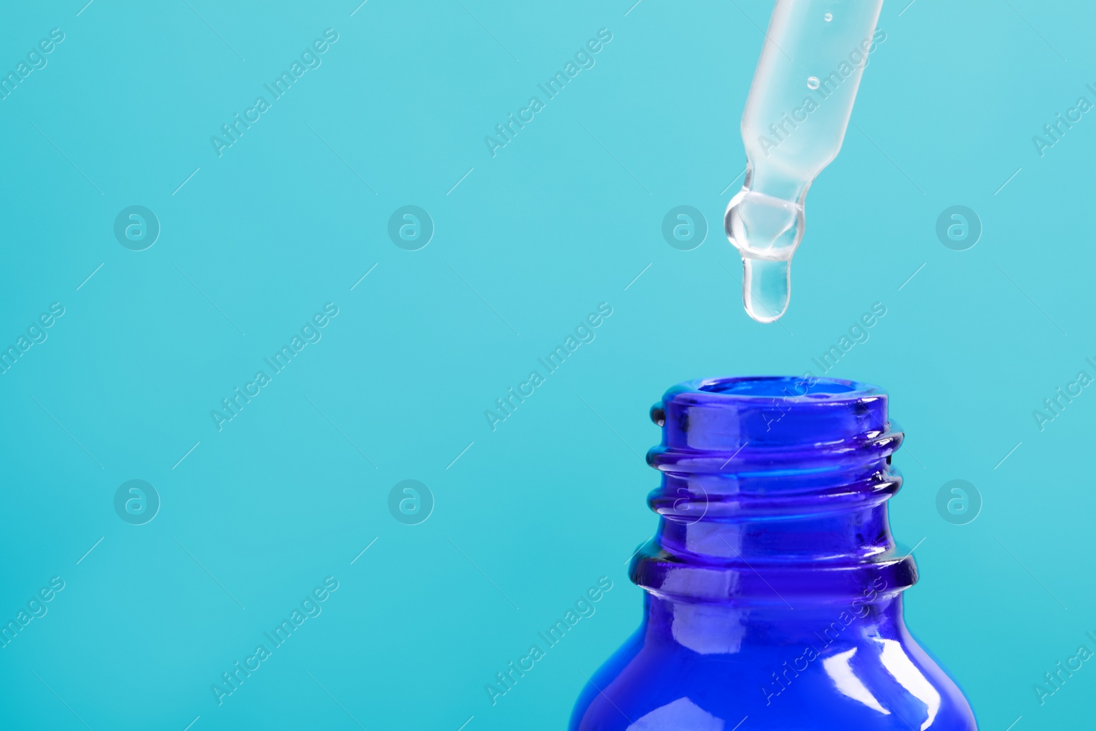 Photo of Dripping serum from pipette into bottle on light blue background, closeup. Space for text