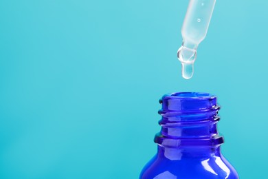 Photo of Dripping serum from pipette into bottle on light blue background, closeup. Space for text