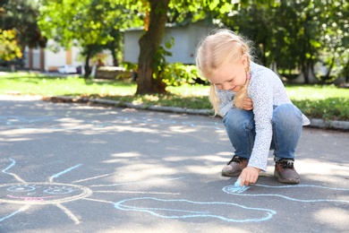 Photo of Little child drawing with colorful chalk on asphalt. Space for text