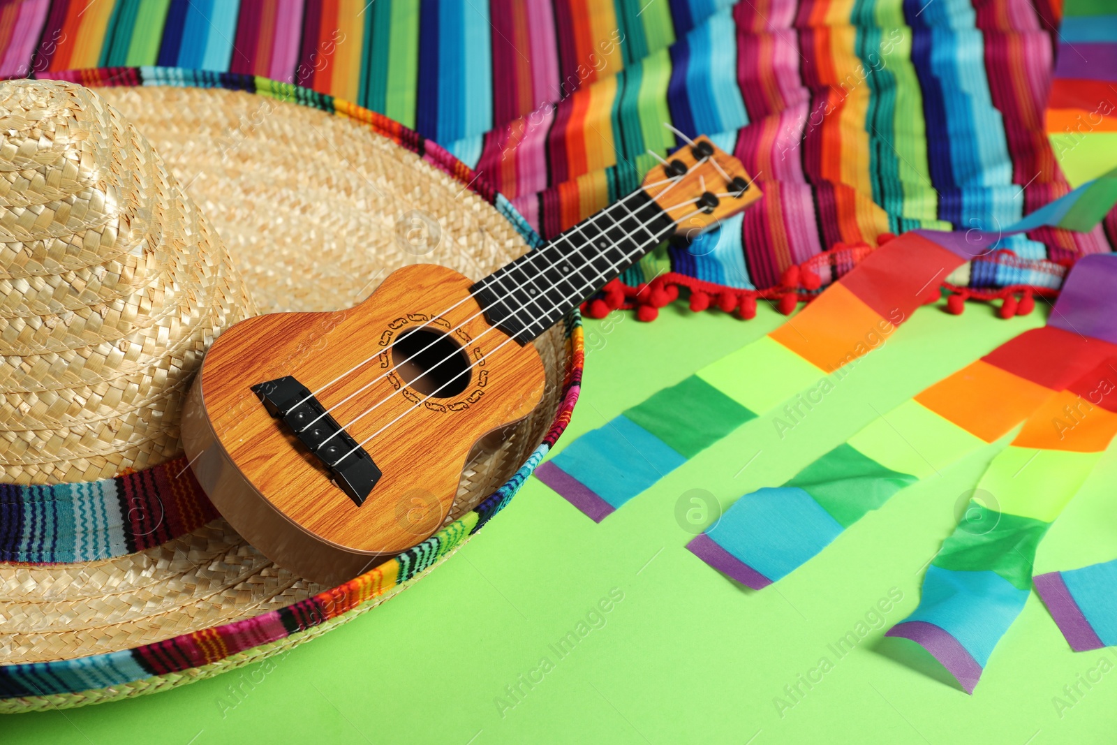 Photo of Mexican sombrero hat and ukulele on green table, closeup