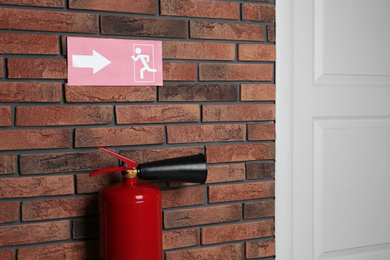 Photo of Fire extinguisher and emergency exit sign on brick wall indoors