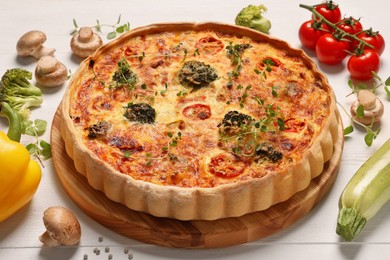 Photo of Delicious homemade vegetable quiche and ingredients on white table