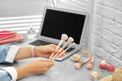 Photo of Young beauty blogger with brushes at light grey marble table, closeup