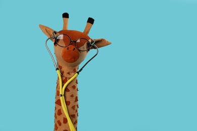 Photo of Toy giraffe with glasses and stethoscope on light blue background, space for text. Pediatrician practice