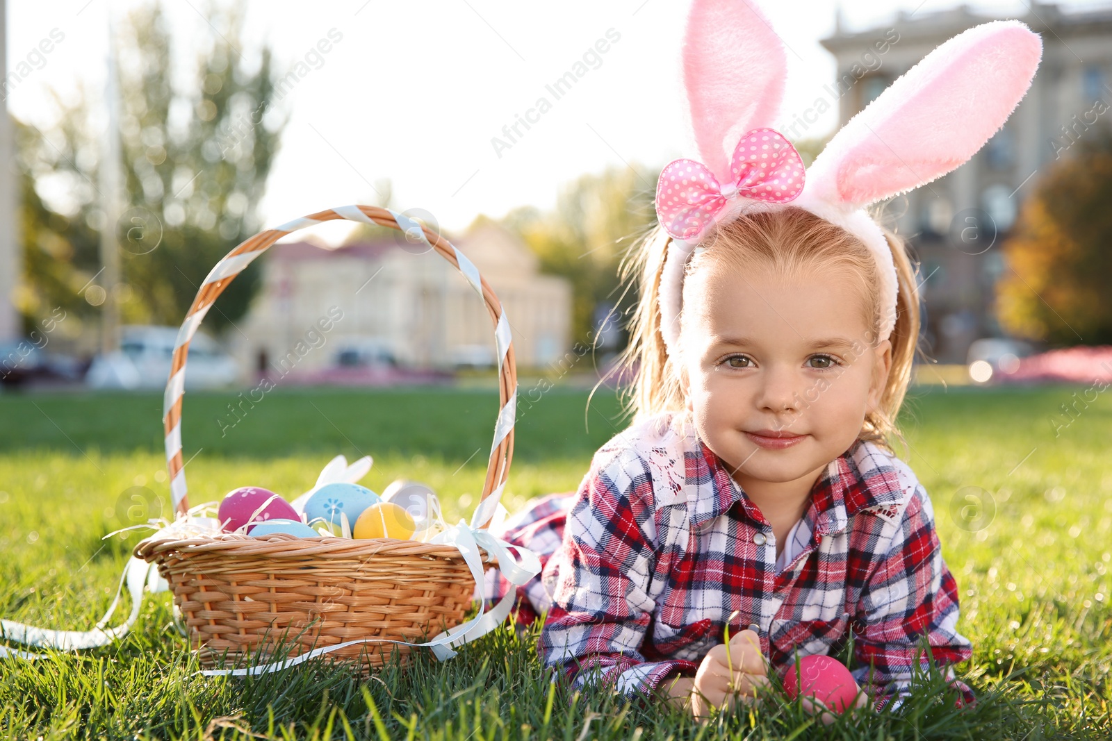 Photo of Cute little girl with bunny ears and basket of Easter eggs in park