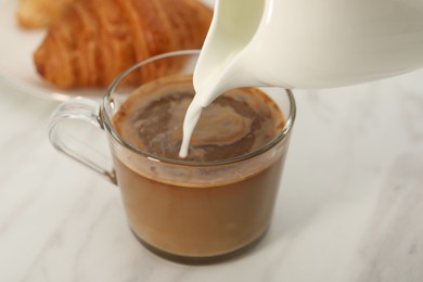 Photo of Pouring milk in coffee at white table, closeup