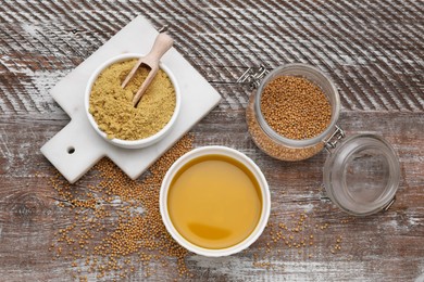 Photo of Bowl of natural oil, mustard seeds and powder on wooden table, flat lay
