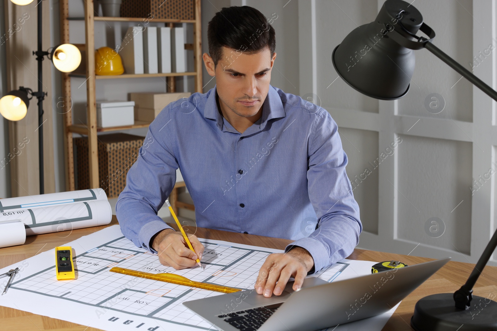 Photo of Architect working with construction drawings and laptop in office