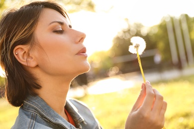 Young woman with dandelion in park on sunny day. Allergy free concept