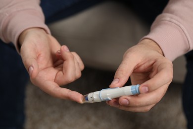 Photo of Diabetes test. Man checking blood sugar level with lancet pen on blurred background, closeup