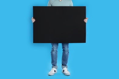 Photo of Man holding blank poster on blue background, closeup