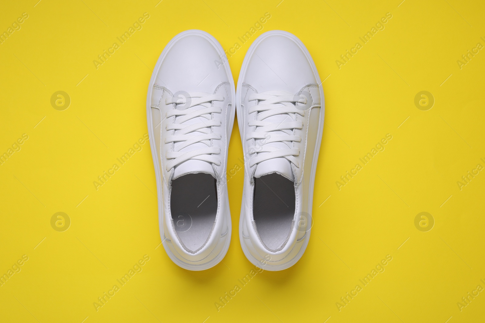 Photo of Pair of stylish white sneakers on yellow background, top view