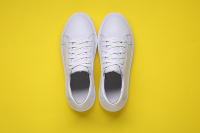 Photo of Pair of stylish white sneakers on yellow background, top view