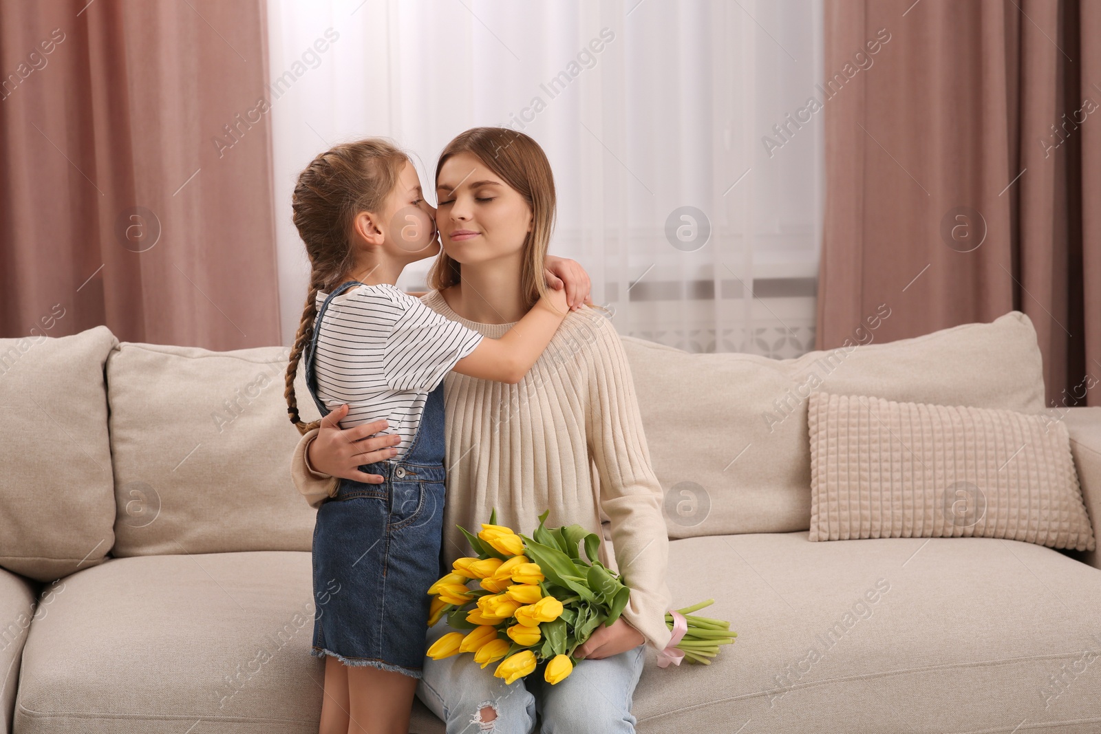 Photo of Little daughter congratulating mom with bouquet of yellow tulips at home. Happy Mother's Day