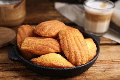 Delicious madeleine cakes in frying pan on wooden table, closeup