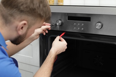 Photo of Professional serviceman repairing modern oven in kitchen