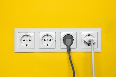 Photo of Power sockets with inserted plugs on yellow wall. Electrical supply