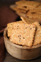 Photo of Cereal crackers with flax and sesame seeds in bowl on wooden table, closeup