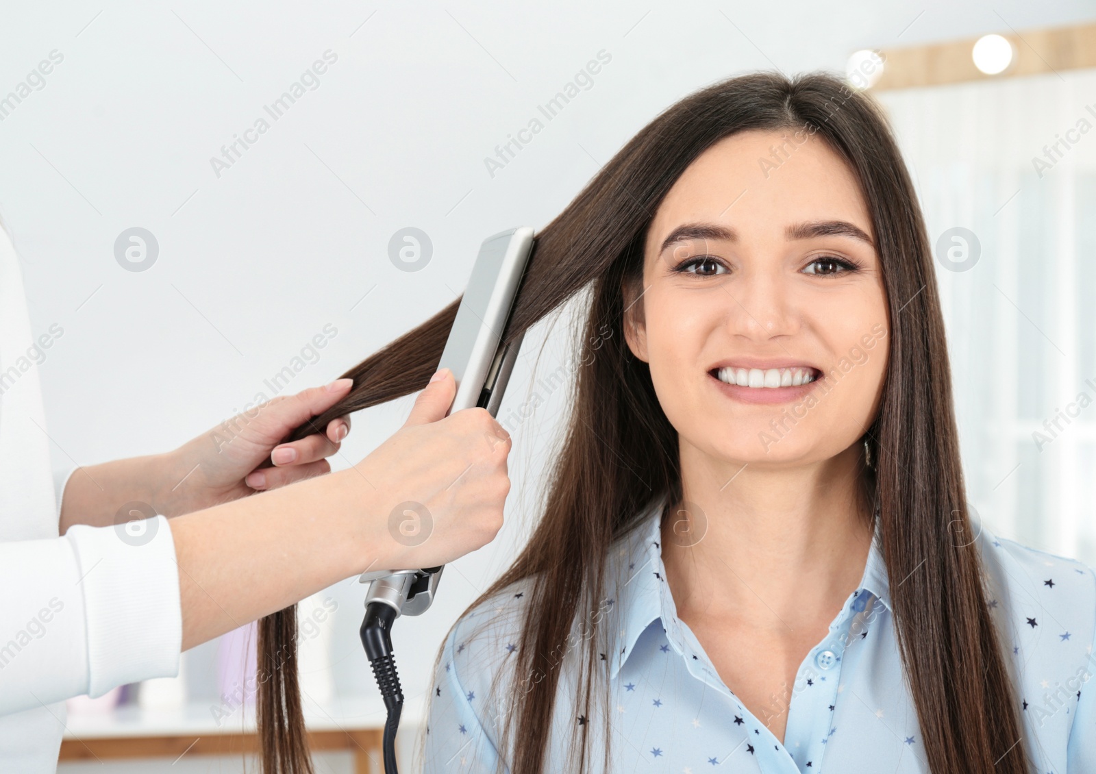 Photo of Hairdresser using modern flat iron to style client's hair in salon