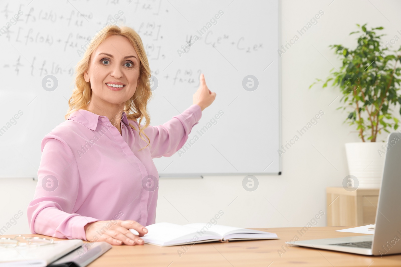 Photo of Teacher giving lesson near laptop at desk in classroom, space for text