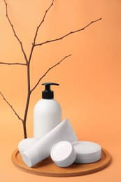 Cosmetic products and decorative twig on orange background