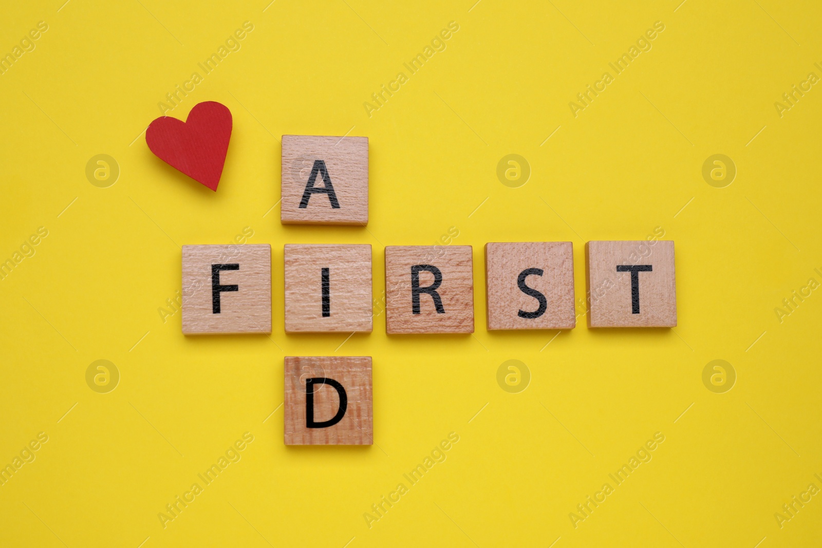 Photo of Words First Aid made of wooden cubes and cardboard heart on yellow background, flat lay