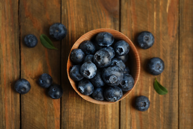 Fresh ripe blueberries in bowl on wooden table, flat lay