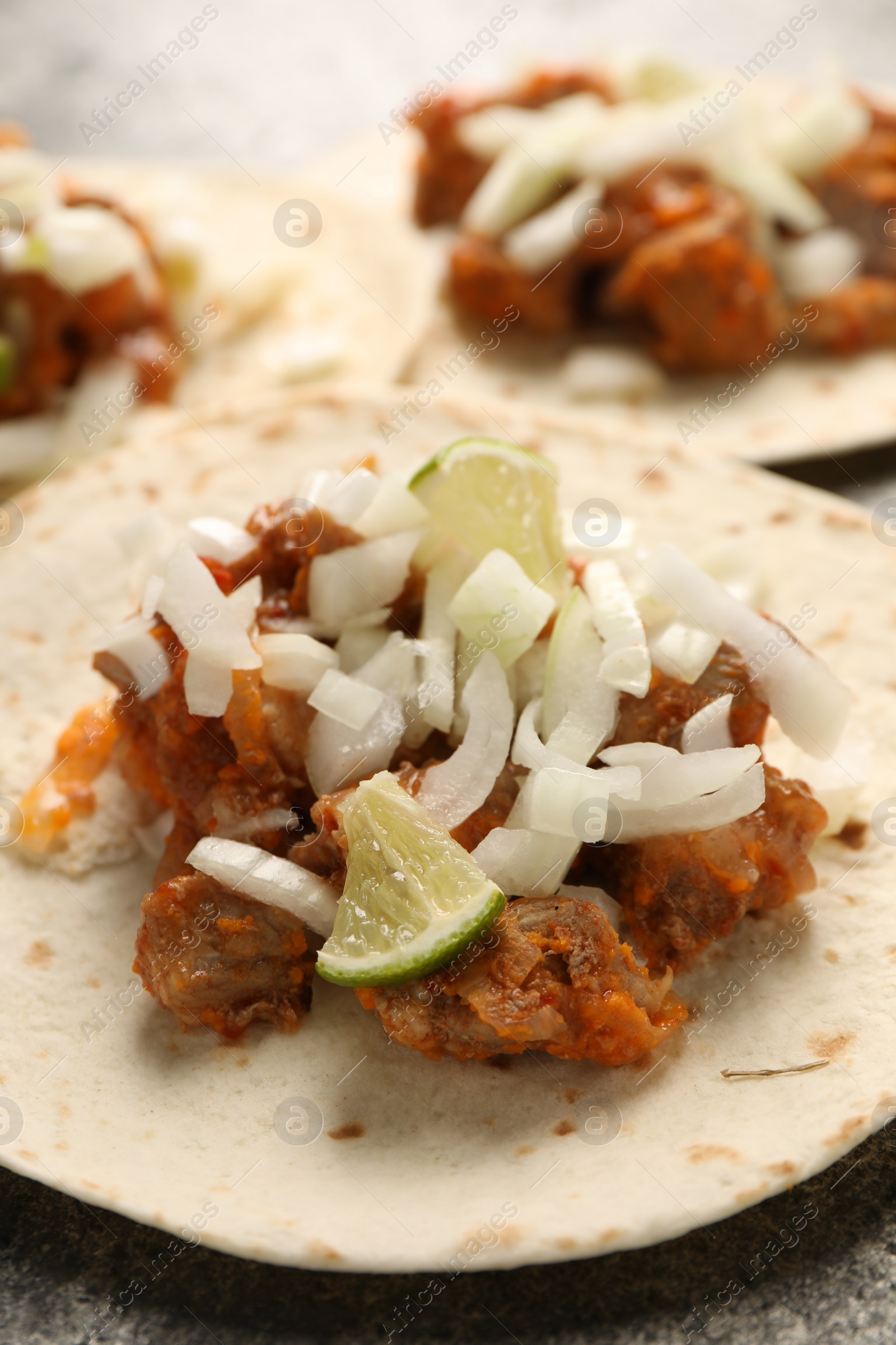 Photo of Delicious tacos with vegetables, meat and lime on grey textured table, closeup