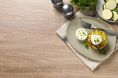Photo of Delicious zucchini fritters with sour cream served on wooden table, flat lay. Space for text
