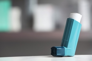 Asthma inhaler on table against blurred background. Space for text