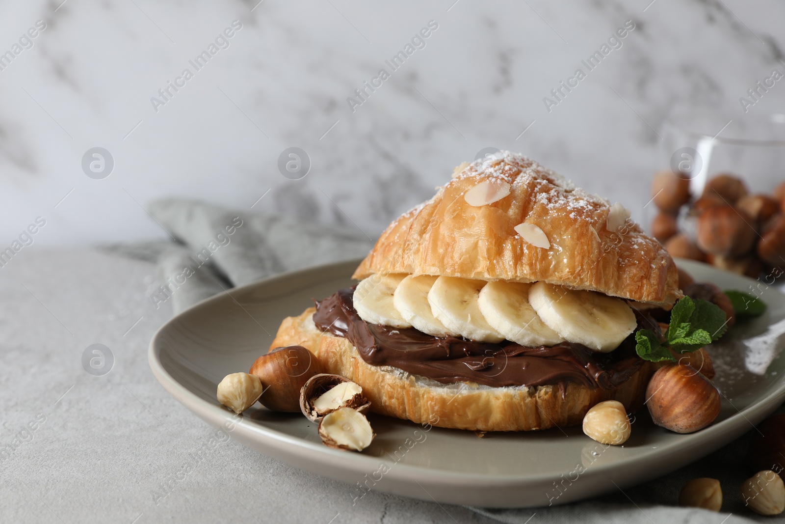 Photo of Delicious croissant with banana, chocolate and hazelnuts on gray table, closeup. Space for text