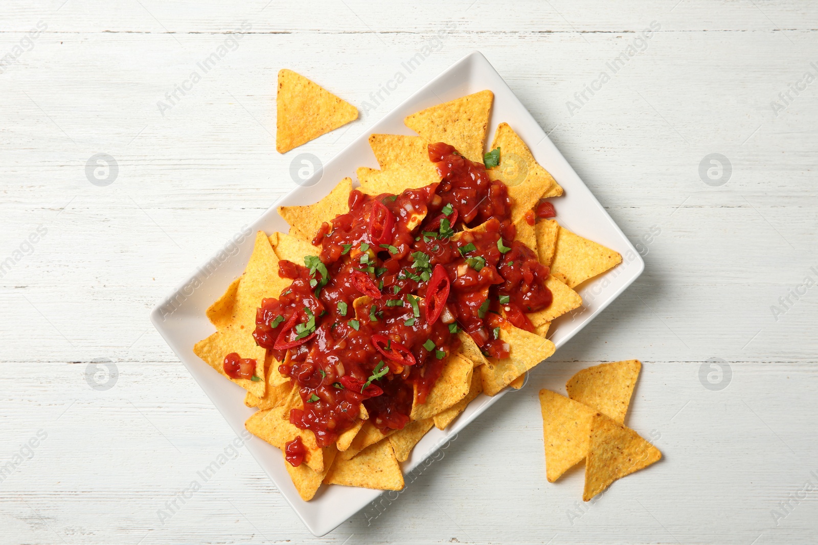 Photo of Plate of delicious mexican nachos chips with salsa sauce on white wooden table, flat lay