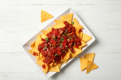 Plate of delicious mexican nachos chips with salsa sauce on white wooden table, flat lay