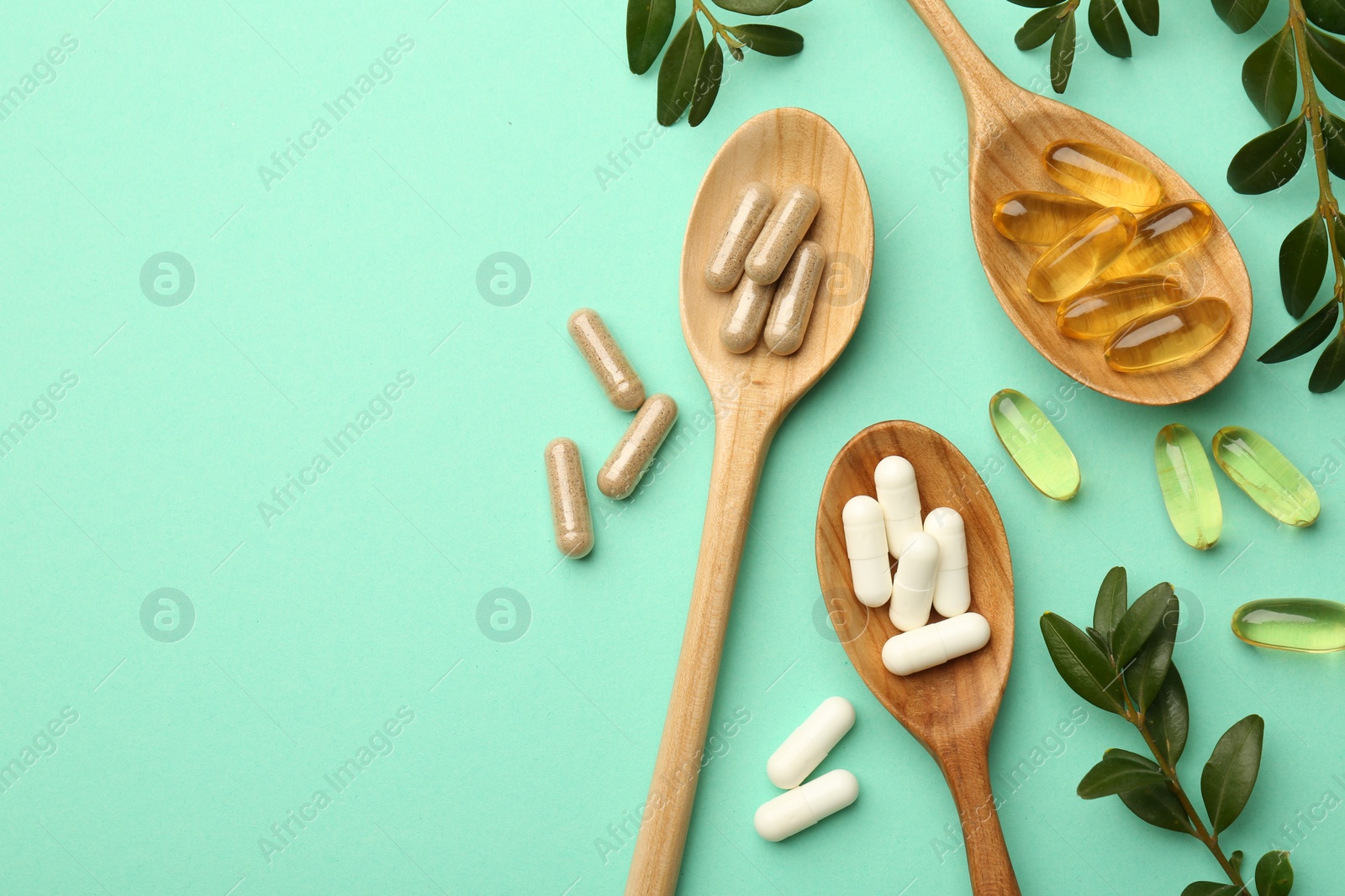 Photo of Different vitamin capsules in spoons and leaves on turquoise background, flat lay. Space for text