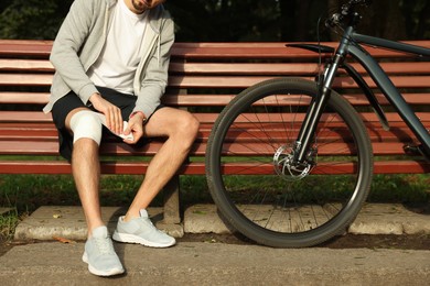 Photo of Man applying bandage onto his knee on wooden bench outdoors, closeup