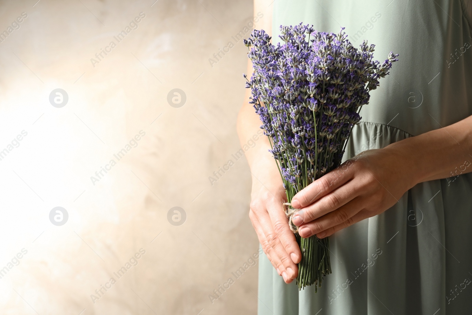 Photo of Woman holding fresh lavender flowers on beige background, closeup. Space for text