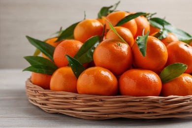 Photo of Fresh ripe juicy tangerines and green leaves on white wooden table, closeup