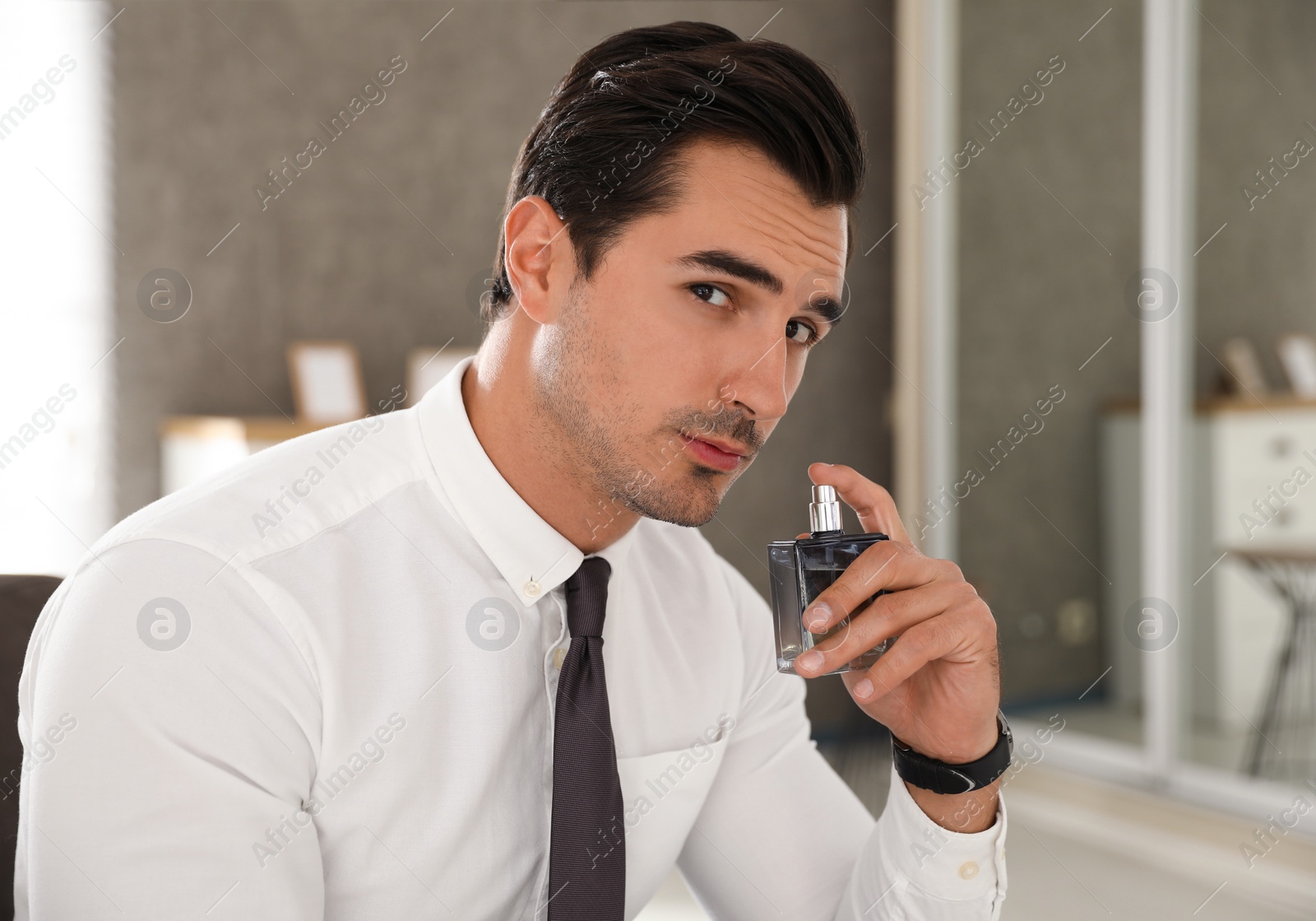 Photo of Handsome young man using luxury perfume indoors