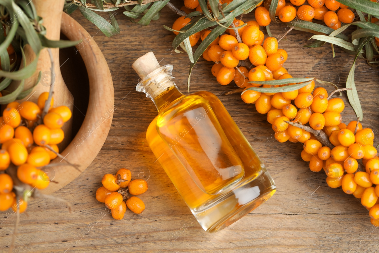 Photo of Natural sea buckthorn oil and fresh berries on wooden table, flat lay