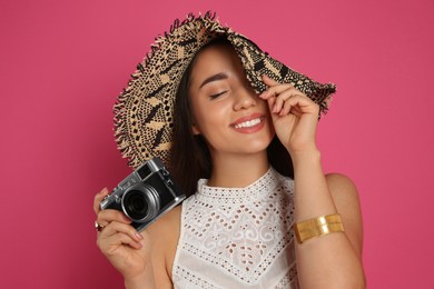 Photo of Beautiful young woman with straw hat and camera on crimson background. Stylish headdress