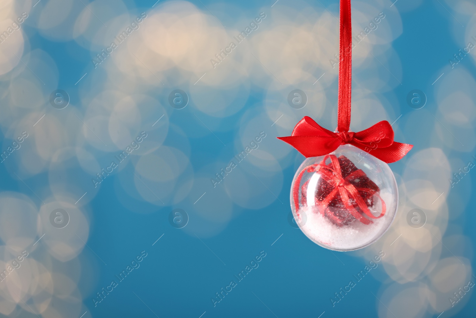 Photo of Decorative snow globe hanging against blurred festive lights, space for text