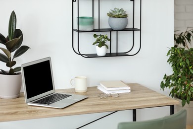 Comfortable workplace with modern laptop on wooden table in room. Interior design