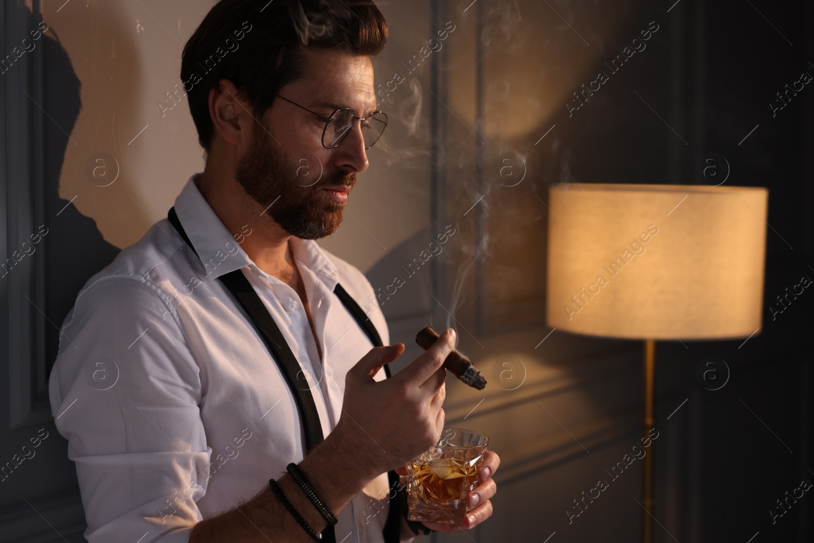 Photo of Handsome man with glass of whiskey smoking cigar at home. Space for text