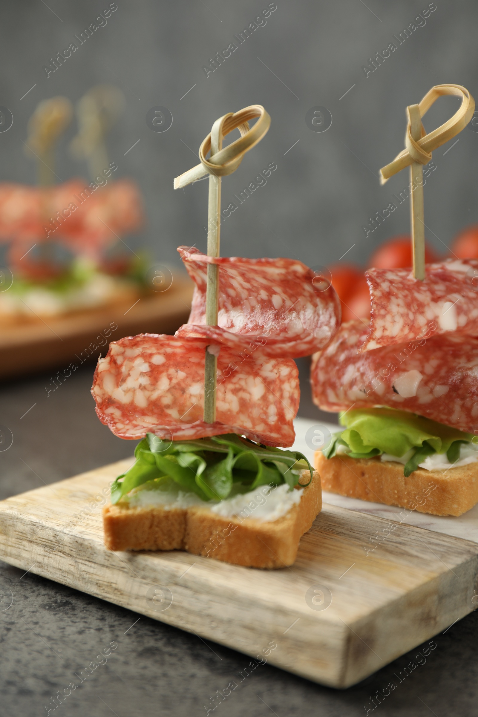 Photo of Tasty canapes with salami, greens and cream cheese on grey table, closeup