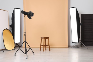 Photo of Beige photo background, stool and professional lighting equipment in studio