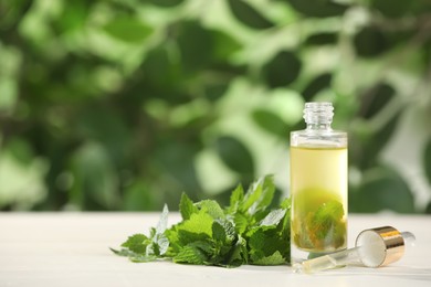 Photo of Glass bottle of nettle oil with dropper and leaves on white table against blurred background, space for text