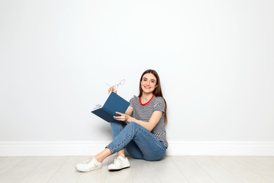 Photo of Young woman reading book on floor near white wall, space for text