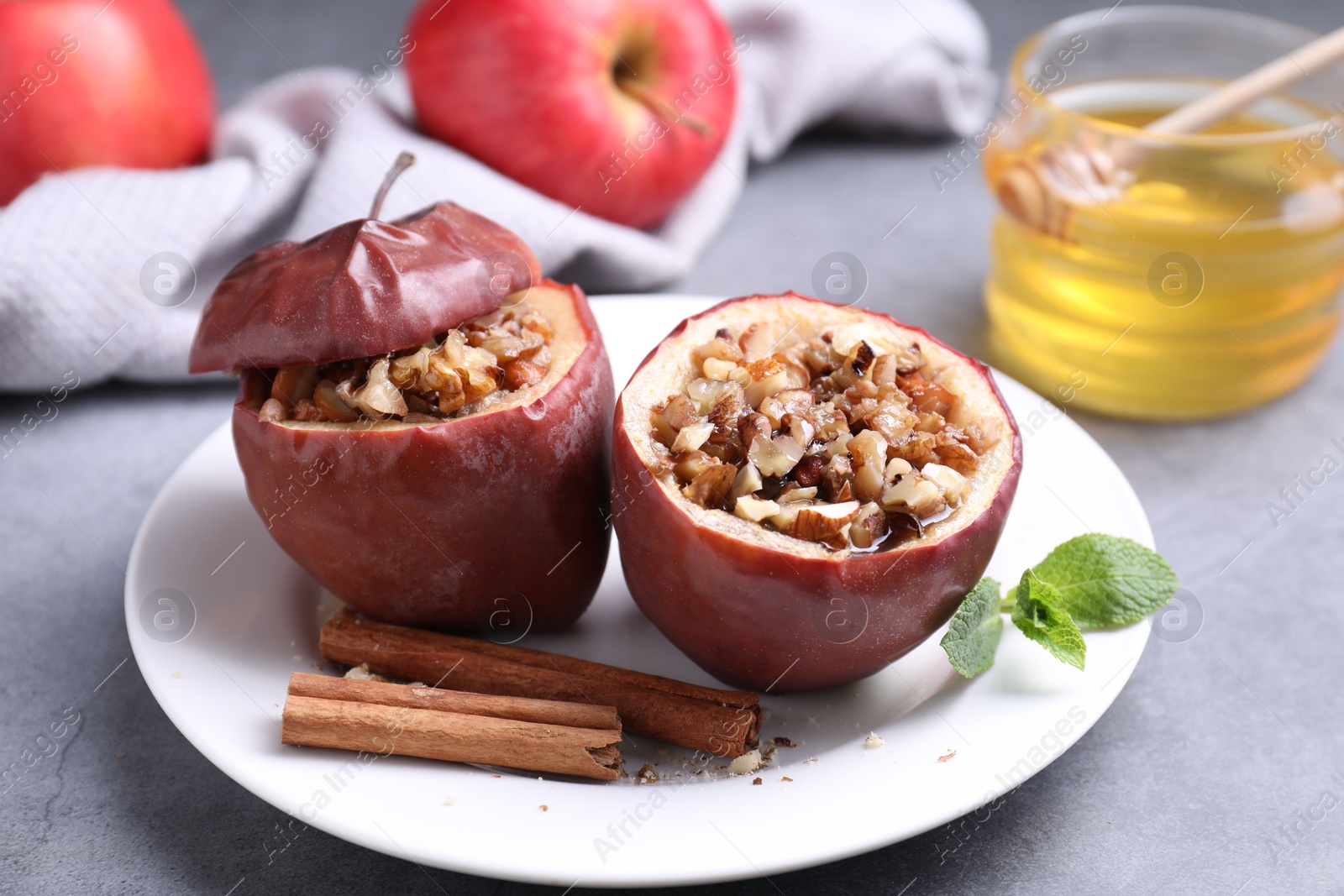 Photo of Tasty baked apples with nuts, honey, cinnamon sticks and mint on gray table, closeup